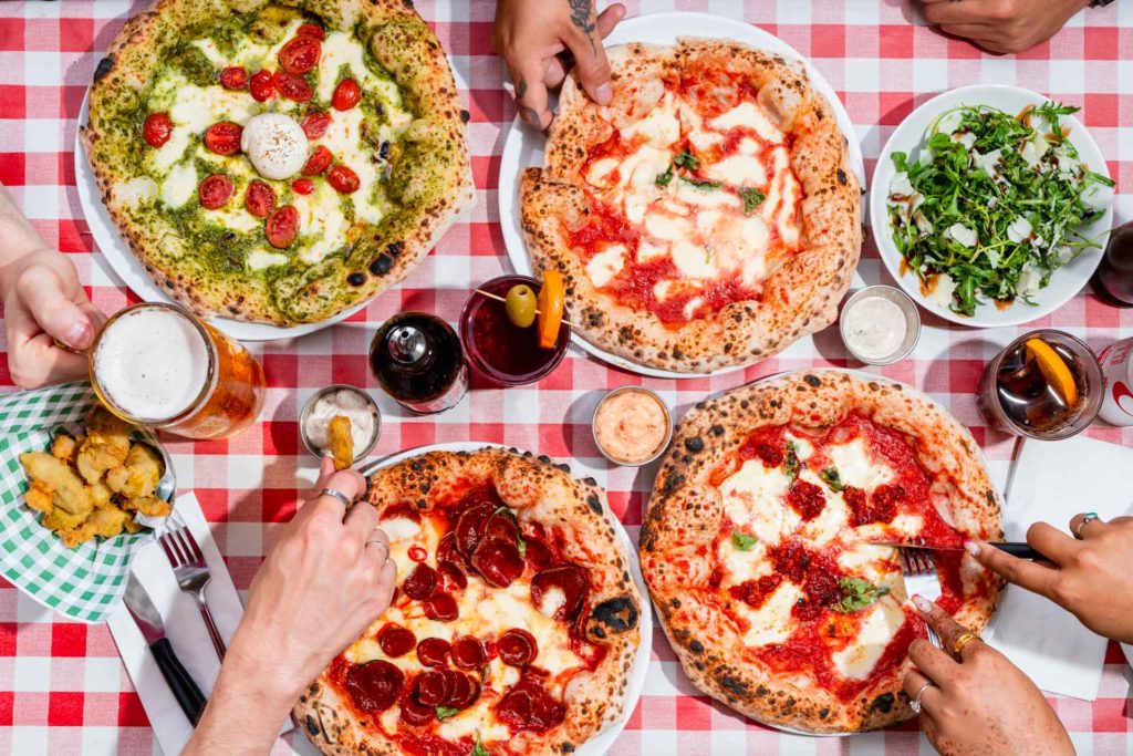 Aerial view of margarita and pepperoni pizzas on a red and white gingham tablecloth. Pizza PILGRIMS